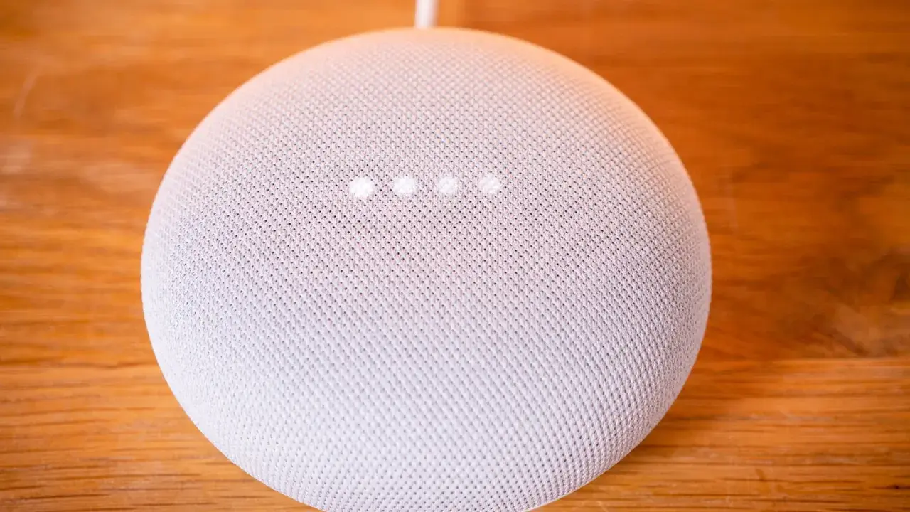 Ein weißer Google Nest Mini auf einem Holztisch. Die vier Lichter zeigen an, dass das Gerät auf Werkseinstellung zurückgesetzt wird.