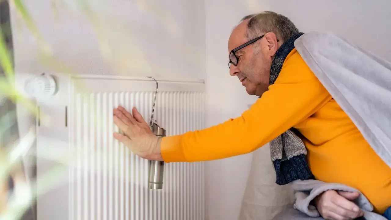 Mann prüft Heizung. Kein warmwasser und heizung wie lange zumutbar? Er ist in Decke gehüllt.