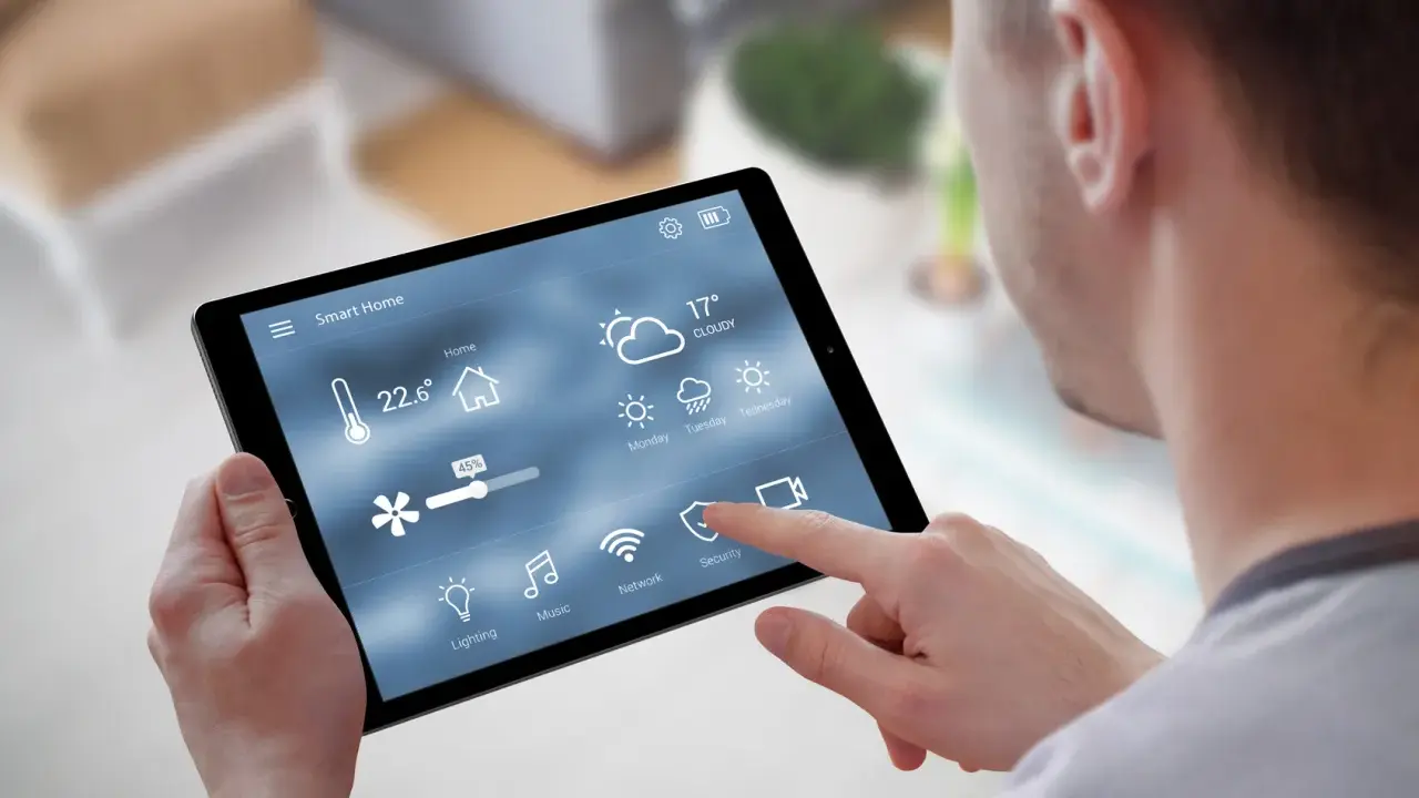Mann steuert Smart Home per Tablet. Temperatur, Wetter & Lüftung sind sichtbar. Über Bluetooth vernetzt.