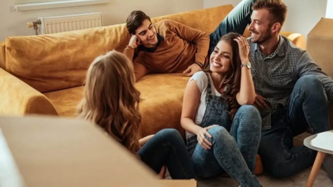 Glückliche Freunde lachen auf dem Boden vor einem Sofa, umgeben von Umzugskartons. Ein privater Vermieter könnte ihnen hier beim Einzug helfen.
