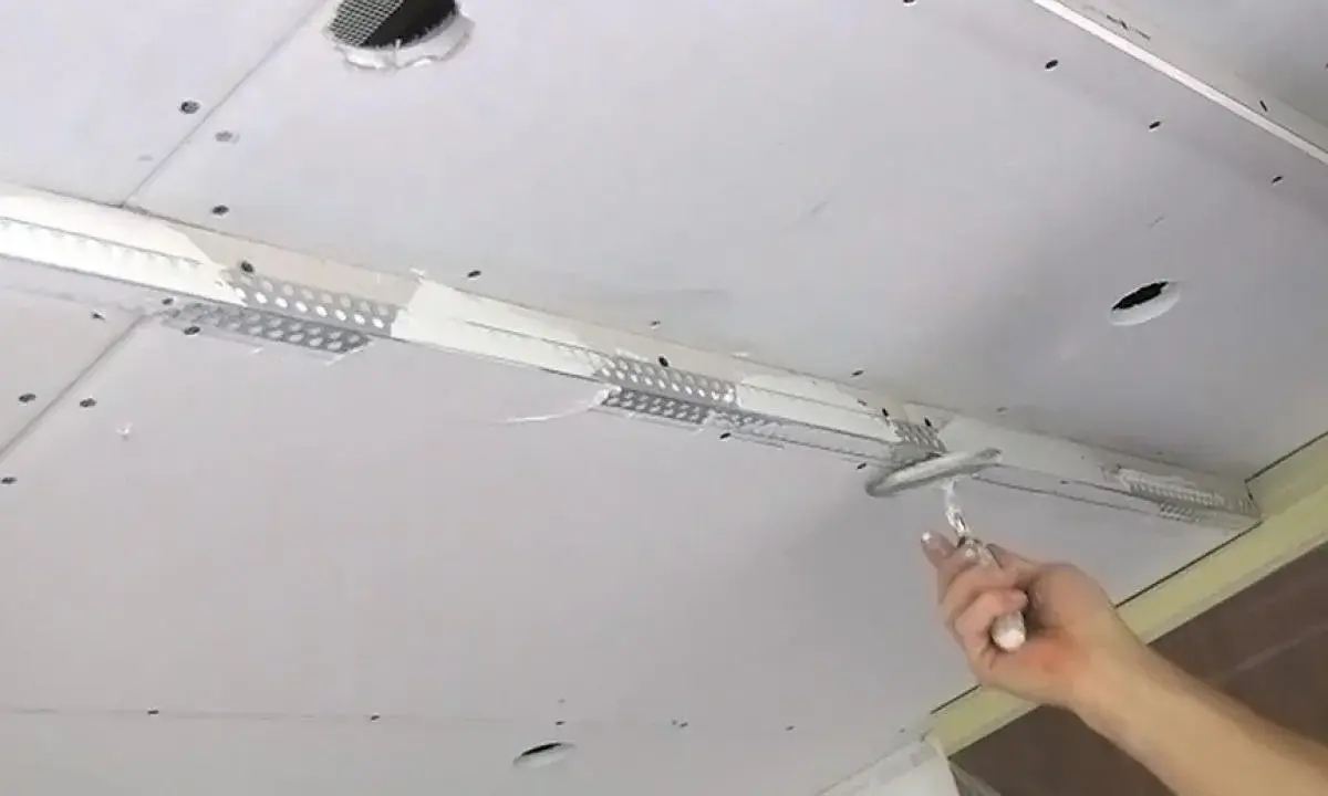Hand glättet mit Spachtel die Naht beim Gipskarton verputzen. Decke mit Lüftungsgitter und Löchern.