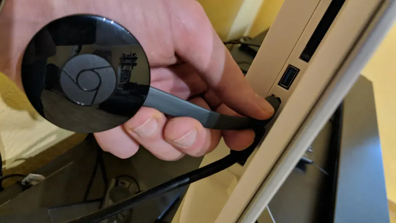 Hand connects a black Chromecast to a USB port on a device, preparing to chromecast mit wlan verbinden.