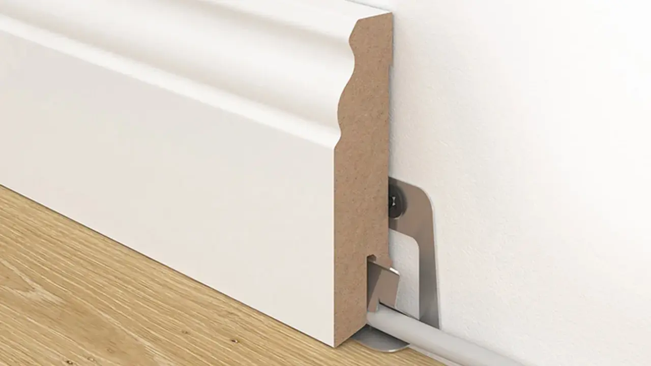 Weiße Sockelleiste mit Kabelkanal, die an der Wand befestigt ist. So kann man Leisten kleben und Kabel verstecken.