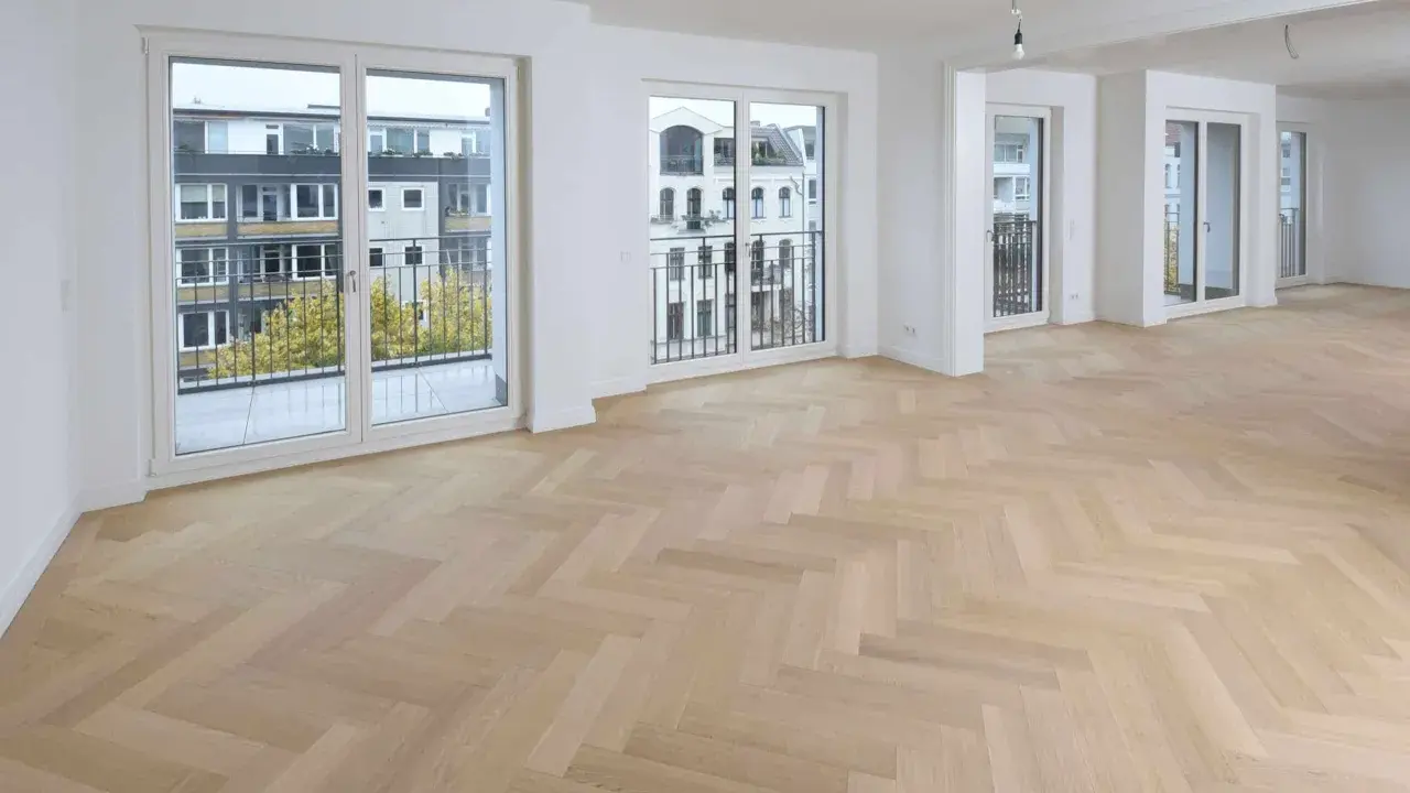 Ein heller Fischgrätenparkettboden, frisch nach dem Parkett schleifen, erstrahlt in einem modernen Wohnraum mit großen Fenstern und Balkonen.
