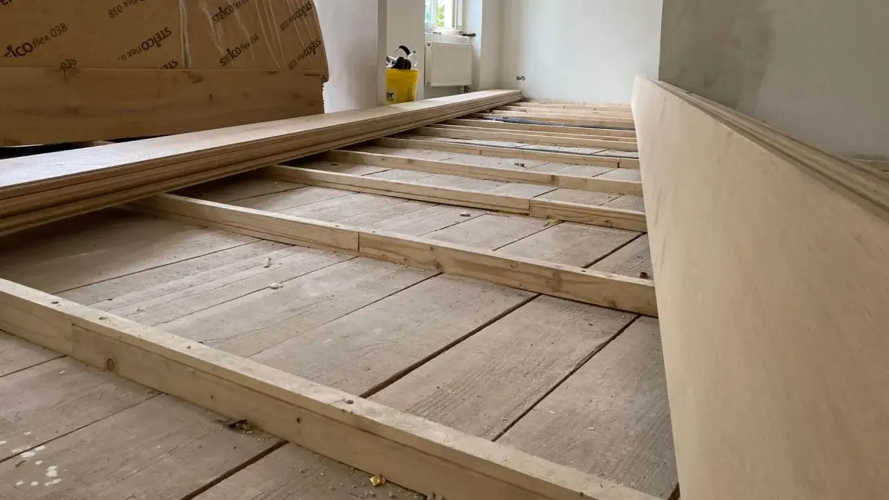 Holzbalken werden auf einem alten Holzboden verlegt, um ihn für eine neue Verkleidung vorzubereiten. So kann man den Boden ausgleichen ohne Ausgleichsmasse.