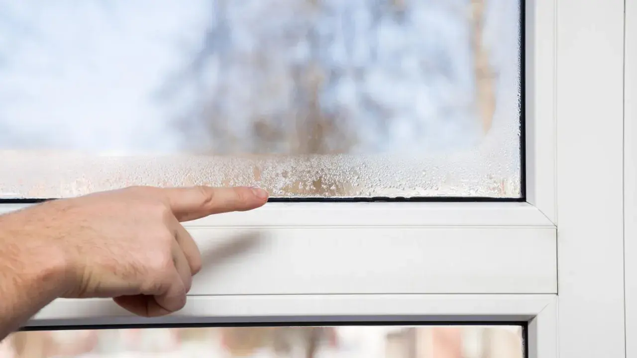 Finger zeigt auf beschlagene Fensterscheibe. Hohe Luftfeuchtigkeit im Raum senken ist wichtig, um Kondensation zu vermeiden.
