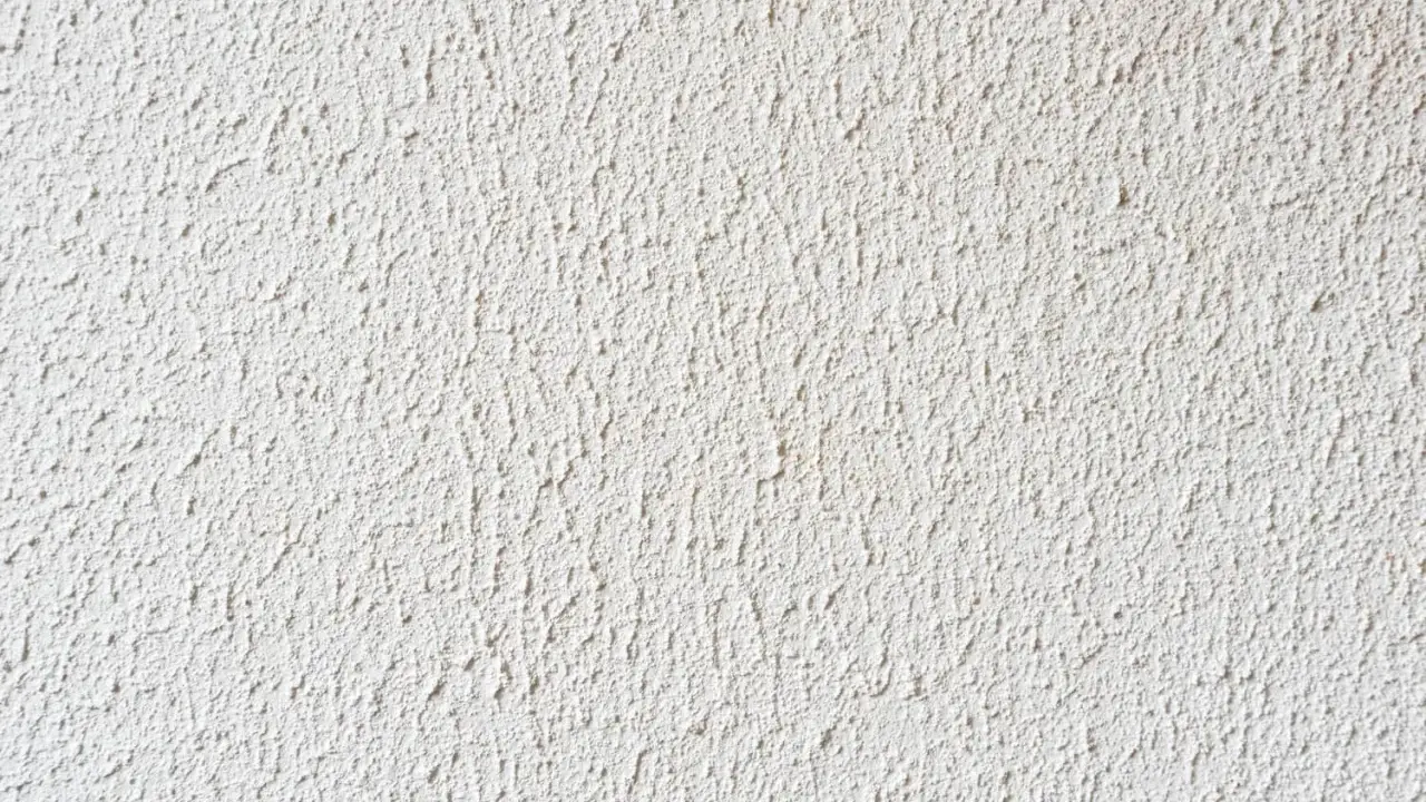 Eine weiße Wand mit feinem Rollputz auf Tapete. Die Struktur ist unregelmäßig und erzeugt ein lebendiges Oberflächenbild.