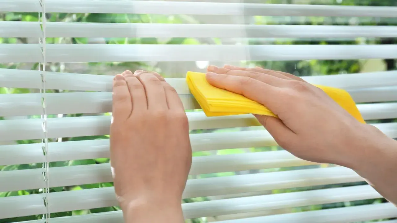Hände reinigen mit gelbem Tuch die Lamellen einer Jalousie.