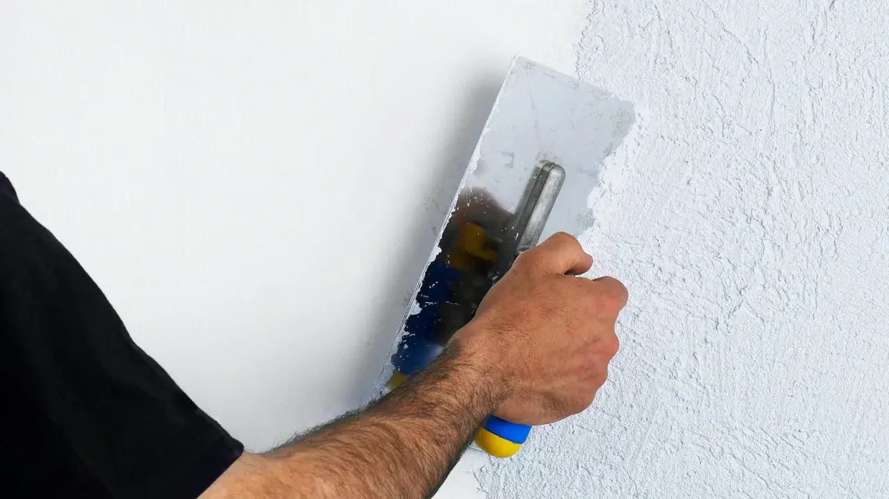 Hand mit Glättekelle bearbeitet eine Wand, um den Putz zu filzen und eine strukturierte Oberfläche zu schaffen.