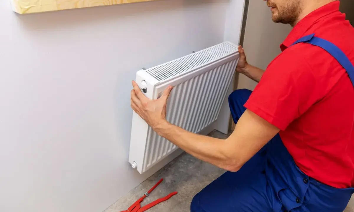 Handwerker montiert Heizkörper. Werkzeug liegt bereit.