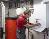 Techniker führt Abgasmessung an Heizung durch. Er bedient das Bedienfeld des modernen Brennwertgeräts.