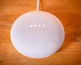 Ein weißer Google Nest Mini auf einem Holztisch. Die vier Lichter zeigen an, dass das Gerät auf Werkseinstellung zurückgesetzt wird.