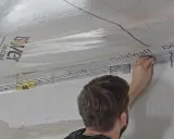 Mann bringt eine Dampfbremse an der Decke an. Die silberne Folie mit dem Isover-Logo wird sorgfältig verklebt.