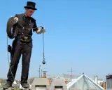 Ein Schornsteinfeger in traditioneller Kleidung mit Zylinder und Seil steht auf einem Dach. Die Reinigung der Kamine ist eine wichtige Schornsteinfeger Pflicht.