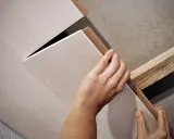 Hände bringen Deckenpaneele an, ohne Unterkonstruktion. Die Paneele werden direkt an die Decke geklebt oder geschraubt.