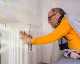 Mann prüft Heizung. Kein warmwasser und heizung wie lange zumutbar? Er ist in Decke gehüllt.