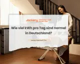 Frau bügelt, während Jackery SolarVault 3 Pro im Hintergrund steht. Die Frage "Wie viel kWh pro Tag sind normal in Deutschland?" wird thematisiert.