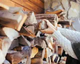 Hände greifen nach Holzscheiten, die für ein Einfamilienhaus gestapelt sind. Die Menge an Holz, die ein Einfamilienhaus benötigt, hängt von vielen Faktoren ab.