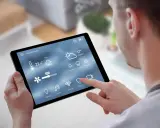 Mann steuert Smart Home per Tablet. Temperatur, Wetter & Lüftung sind sichtbar. Über Bluetooth vernetzt.
