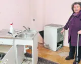 Ältere Frau mit Sauerstoffgerät und Krückstock zeigt auf schmutzigen Herd. Sie fühlt sich vom Vermieter schikaniert.
