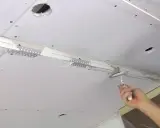 Hand glättet mit Spachtel die Naht beim Gipskarton verputzen. Decke mit Lüftungsgitter und Löchern.