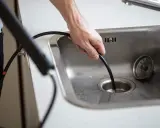 Mann versucht, ein verstopftes Waschbecken mit einer Rohrreinigungsspirale zu befreien.