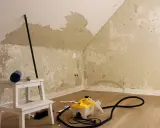 Raufasertapete entfernen: Dampfreiniger und Werkzeug auf dem Boden, die Wand ist teilweise abgerissen.