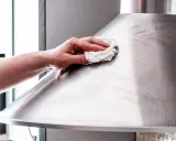 Hand poliert mit einem Tuch eine Dunstabzugshaube aus Edelstahl, um sie zum Glänzen zu bringen.