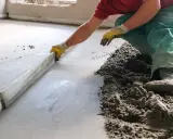 Mann verlegt Estrich mit einer Richtlatte.