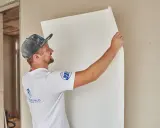 Maler tapeziert Malervlies an einer Wand.