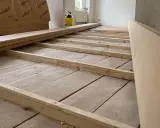 Holzbalken werden auf einem alten Holzboden verlegt, um ihn für eine neue Verkleidung vorzubereiten. So kann man den Boden ausgleichen ohne Ausgleichsmasse.
