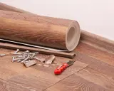 Materialien für das Linoleum verlegen: eine gerollte Bodenbelagsbahn, Sockelleisten, Dübel, Schrauben und ein Cuttermesser liegen bereit.