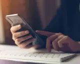 Person tippt auf Smartphone, weil hey Google funktioniert nicht. Tastatur und Maus im Vordergrund.