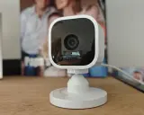Kompakte Überwachungskamera mit Blink-Logo, die als Alexa-kompatible Alarmanlage dient. Im Hintergrund sind Familienfotos zu sehen.