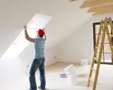 Mann misst eine Dachschräge für eine **leichtbauwand in Mietwohnung erlaubt**. Werkzeug und Farbeimer stehen bereit.