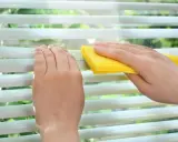 Hände reinigen mit gelbem Tuch die Lamellen einer Jalousie.