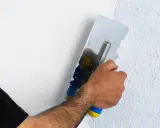 Hand mit Glättekelle bearbeitet eine Wand, um den Putz zu filzen und eine strukturierte Oberfläche zu schaffen.