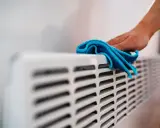Hand wischt über Heizkörper. Die Heizung wird nicht warm, Rohre kalt.