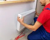 Handwerker montiert Heizkörper. Werkzeug liegt bereit.