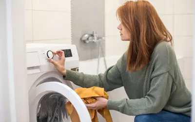 Frau stellt Waschmaschine ein, achtet auf wasserverbrauch. Sie hält ein gelbes Kleidungsstück.