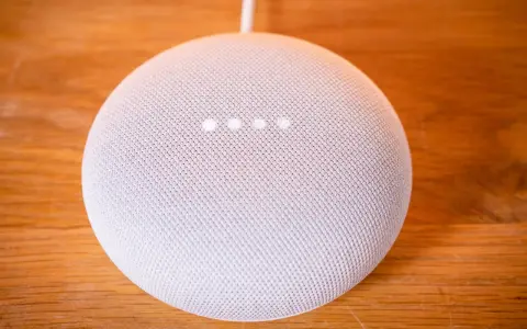 Ein weißer Google Nest Mini auf einem Holztisch. Die vier Lichter zeigen an, dass das Gerät auf Werkseinstellung zurückgesetzt wird.