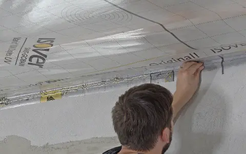 Mann bringt eine Dampfbremse an der Decke an. Die silberne Folie mit dem Isover-Logo wird sorgfältig verklebt.