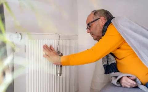 Mann prüft Heizung. Kein warmwasser und heizung wie lange zumutbar? Er ist in Decke gehüllt.