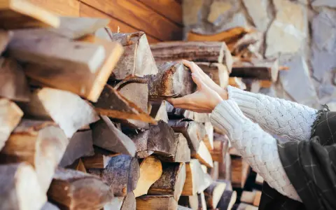 Hände greifen nach Holzscheiten, die für ein Einfamilienhaus gestapelt sind. Die Menge an Holz, die ein Einfamilienhaus benötigt, hängt von vielen Faktoren ab.