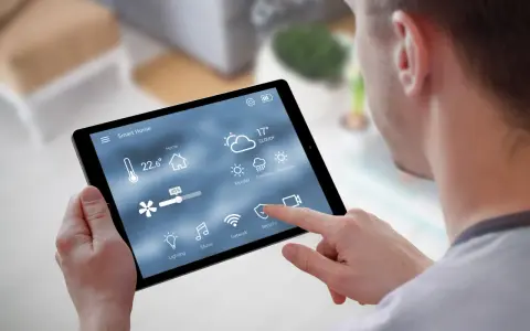 Mann steuert Smart Home per Tablet. Temperatur, Wetter & Lüftung sind sichtbar. Über Bluetooth vernetzt.