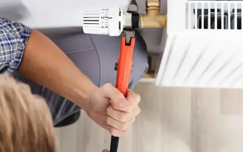 Hand mit Rohrzange dreht am Thermostatventil, um es abzuschrauben. Heizkörper wird repariert.