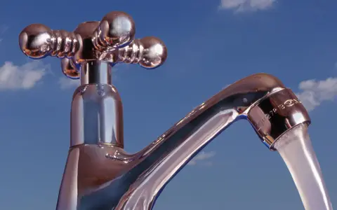 Chromhahn mit laufendem Wasser vor blauem Himmel. Der Wasserdruck ist gut, die **druck wasserleitung** liefert kräftig.
