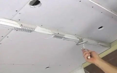 Hand glättet mit Spachtel die Naht beim Gipskarton verputzen. Decke mit Lüftungsgitter und Löchern.