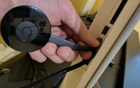 Hand connects a black Chromecast to a USB port on a device, preparing to chromecast mit wlan verbinden.