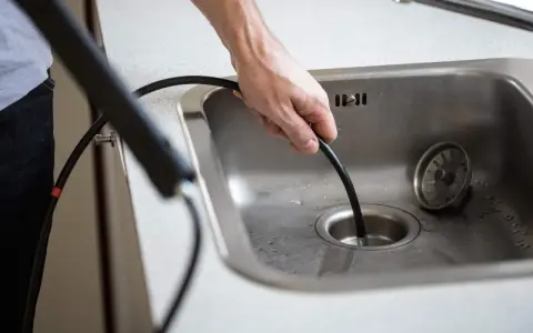 Mann versucht, ein verstopftes Waschbecken mit einer Rohrreinigungsspirale zu befreien.